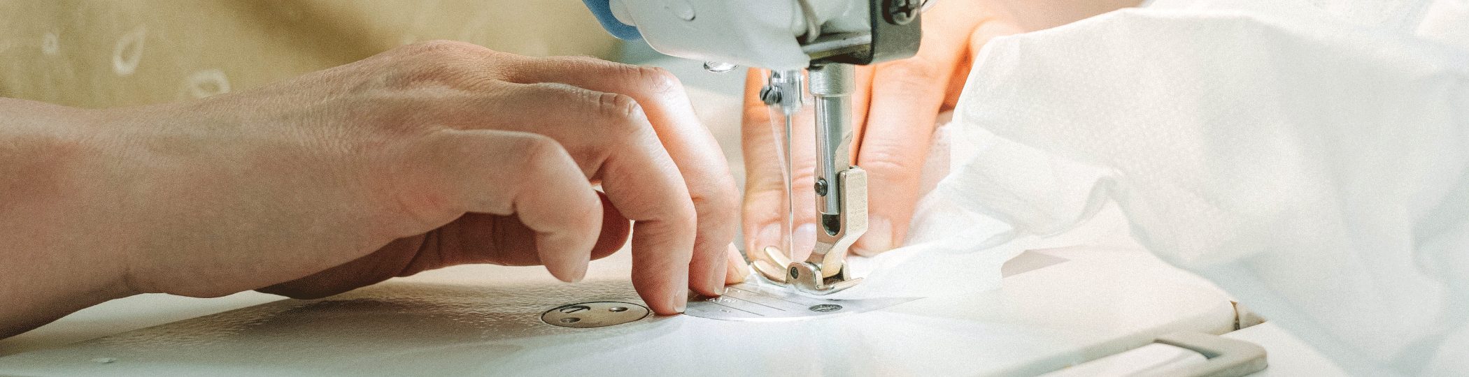 Hands guiding white fabric through a sewing machine